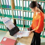 Woman standing over a Canon DR-M160II scanning various sized documents